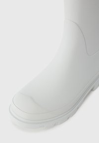 White rubber boot with a smooth, glossy texture, rounded toe, and a treaded outsole for grip. Seamless design with no visible hardware.