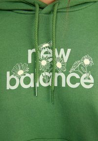 Felpa verde con il logo "new balance" e grafiche floreali, che evidenzia un design casual e alla moda.