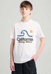Valkoinen puuvillapaita, jossa on sininen aalto- ja keltainen aurinkografiikka sekä teksti "California Making Waves". Yksinkertainen crew neck -muotoilu, lyhyet hihat.
