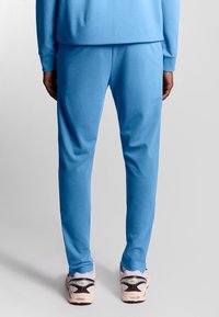 Blauwe joggingbroek van zachte stof, met een relaxte pasvorm en een elastische tailleband, gedragen met lichtgekleurde sportschoenen.