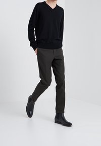 Maglione nero a v collo, aderente con maniche lunghe, abbinato a pantaloni sartoriali verde oliva scuro e stivali neri lucidi alla caviglia.