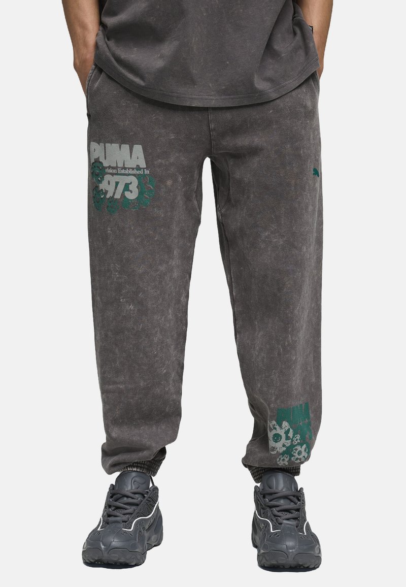 Pantalones jogger de mezcla de algodón grises con puños elásticos. Presenta un logo gráfico en color teal de "PUMA" y un diseño floral en la pierna izquierda.