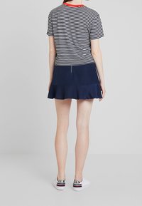 Camiseta a rayas en azul marino y blanco con cuello rojo, combinada con una falda acampanada en azul marino. El conjunto se completa con zapatillas blancas con acentos metálicos.