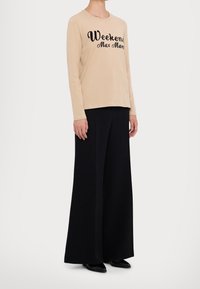Beige Langarmshirt mit schwarzem Kursive-Druck "Weekend Max Mara", kombiniert mit weiten schwarzen Hosen und schwarzen spitzen Schuhen.