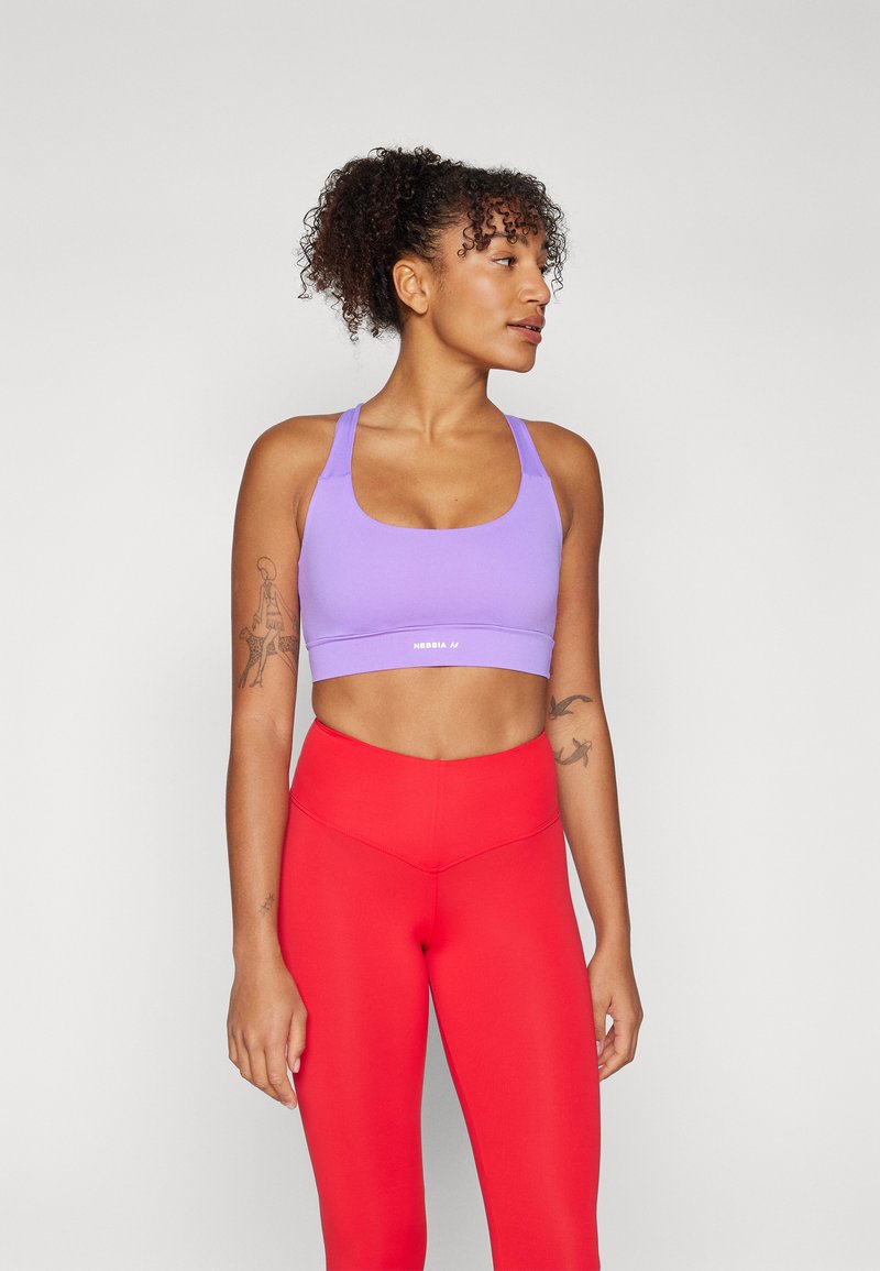 Top deportivo morado corto con escote cuadrado y tirantes anchos, combinado con mallas rojas de tiro alto. Textura suave, con mínima visibilidad de la marca.