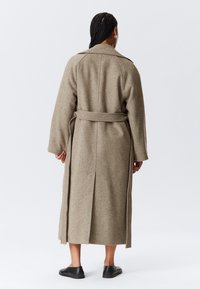 Trenchcoat van wolmix in lichtbruin, met lange mouwen, een tailleband en een achtersplit voor bewegingsvrijheid. Effen textuur zonder versieringen.