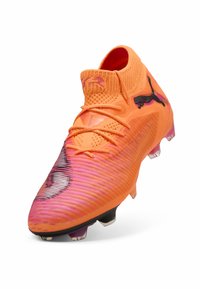 Scarpa da calcio arancione brillante con una tomaia texturizzata, caratterizzata da accenti neri del logo e un design sfumato in rosa. Suola con tacchetti per una migliore aderenza.