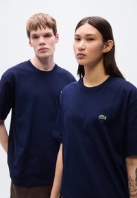 Μπλε βαμβακερά T-shirts σε ναυτικό μπλε χρώμα με μικρό, πράσινο κεντητό λογότυπο κροκόδειλου Lacoste στο αριστερό στήθος. Κλασική γραμμή με στρογγυλές λαιμόκοψεις.