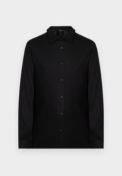 Μαύρο πουκάμισο με μακριά μανίκια και κουμπιά, με κλασικό γιακά και μικρό, διακριτικό λογότυπο στο αριστερό μέρος του στήθους.