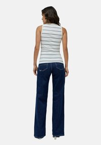 Top de tirantes a rayas en blanco y azul marino, combinado con unos jeans de pierna ancha en azul oscuro, mostrando una silueta ajustada y un estilo casual.