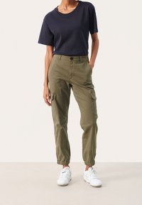 Marinblå bomulls t-shirt med korta ärmar, i kombination med olivgröna cargobyxor som har sidofickor och elastiska muddar. Bärs med vita sneakers.