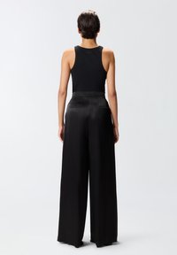 Top nero senza maniche realizzato in un tessuto liscio, abbinato a pantaloni neri a vita alta e gamba larga con un design sartoriale e tasche posteriori.
