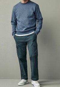 Felpa in cotone blu a girocollo abbinata a pantaloni cargo verde scuro con tasche laterali, completata da sneakers bianche.
