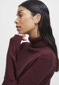 Burgundin turtleneck neule pehmeässä neuloksessa, jossa on ribbireunukset hihansuissa ja kauluksessa. Hieno rakenne, istuva siluetti ja rento muotoilu.
