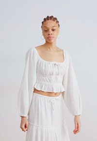 Valkoinen, kuvioitu crop-top, jossa on puffihihoja ja peplum-helma, yhdistettynä pitkäksi hameeksi, jossa on nyörikiristysvyötärö.