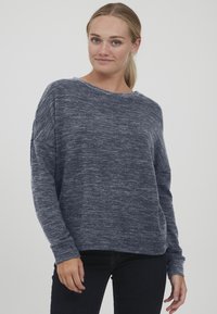 Mørkeblå, teksturert genser med løs passform, bred utringning og lange ermer. Designet har subtile fargeforskjeller og ribbestrikkede mansjetter.