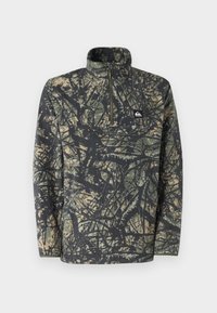 Fleece pullover dalam pola kamuflase dengan warna hitam, hijau, dan coklat muda; dilengkapi dengan kerah seperempat zip dan merek di dada.