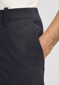 Dunkelgrau kurzer Rock mit glatter Textur, geradem Taillengummi und seitlichem Taschen, mit sichtbaren Nähdetails.