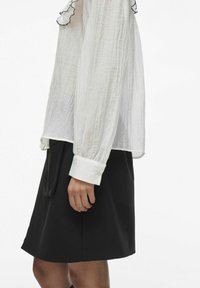 Blusa blanca ligera con acentos negros con volantes en el escote y los puños, combinada con una falda negra a la altura de la rodilla.
