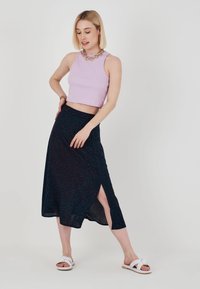 Lila räfflad croptop, marinblå kjol med röd och teal abstrakt mönster, och vita sandaler. Kjolen har en sidoklyfta. Guld kedjearmband.