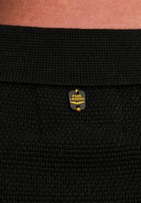 Zwart gebreid stof met een gestructureerd patroon, voorzien van een klein zwart en gouden 'PME Legend' label gestikt op de kraag.