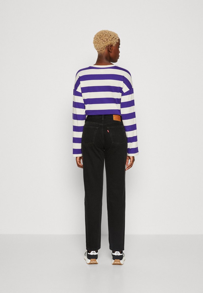 Pantalones de mezclilla negros con un corte recto, combinados con una camisa de rayas morada y blanca de manga larga, visto desde atrás.