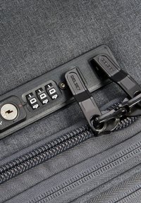 Graue Stofftasche mit einem Kombination-Schlossmechanismus, zwei schwarzen Reißverschlussgriffen und strukturierten Details auf der Oberfläche und dem Reißverschluss.