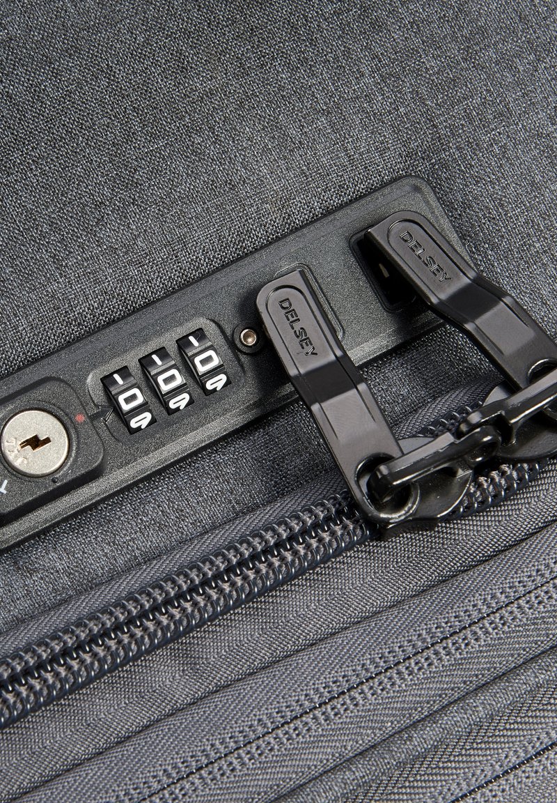 Graue Stofftasche mit einem Kombination-Schlossmechanismus, zwei schwarzen Reißverschlussgriffen und strukturierten Details auf der Oberfläche und dem Reißverschluss.