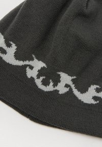 Tessuto a maglia nero con un motivo astratto simile a fiamme bianche vicino al bordo, che mostra una texture dettagliata e pieghe morbide.