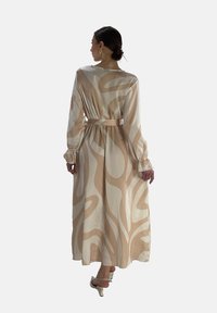 Robe longue beige ornée d'un motif tourbillonnant dans une teinte plus claire. Fabriquée en tissu doux, avec des manches longues et un détail de taille nouée.
