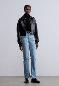 Crna kožna skraćena jakna s ovratnikom, uparena s crnim rolkom, svijetloplavim trapericama i crnim cipelama za odijelo. Suptilni detalji teksture.