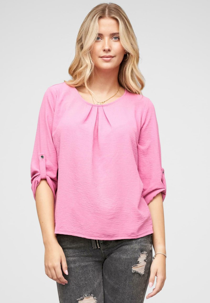 Blusa rosa a maniche lunghe realizzata in un tessuto testurizzato, con scollatura rotonda e dettagli plissettati, maniche arrotolate fissate da bottoni.
