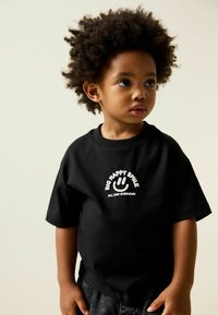 Black cotton t-shirt with short sleeves, featuring white text and smiley graphic on the front. Soft texture and relaxed fit.