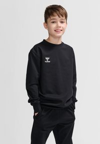 Felpa nera a maniche lunghe e colletto rotondo, con un piccolo logo "hummel" bianco sul petto. Tessuto di cotone liscio, vestibilità comoda.