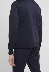 Námořnická modrá sportovní mikina s dlouhými rukávy, žebrovanými manžetami a lemem, vyrobená z hladkého materiálu, s minimalistickým designem a bez viditelných log.