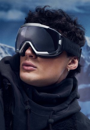 Skijaške naočale za snijeg s tamnim toniranim staklom, srebrnim detaljima i podesivim crnim remenom s logotipom "HAW". Vidljiv je topao crni flisni ovratnik.