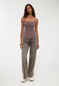 Top fitted di un delicato colore malva con spalline sottili, abbinato a jeans grigi a vita alta con gamba larga e sneakers bianche. Tessuto dal texture morbida.