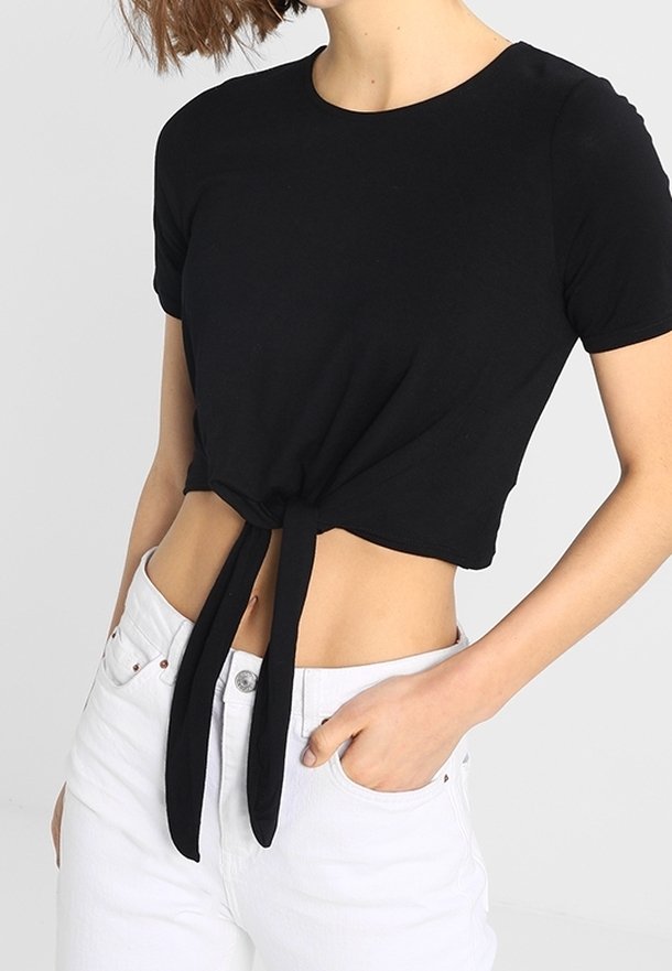 Černé krátké tričko s krátkými rukávy, které má detail uzlu na přední straně. Nosené s bílými džíny s vysokým pasem, bavlněný materiál, hladká textura.