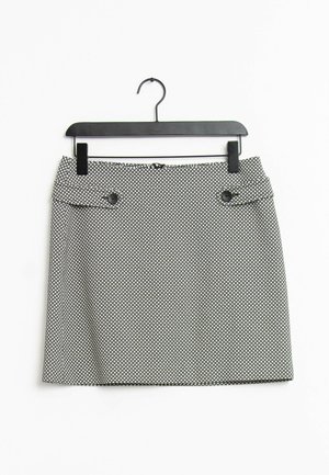 Jupe pour femme à motif noir et blanc avec des pans boutonnés à l'avant, suspendue sur un cintre noir contre un fond blanc.