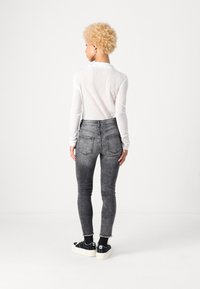 Jean skinny gris taille haute avec une finition délavée, associé à un haut à manches longues côtelé blanc. Baskets à plateforme noires avec des semelles blanches.