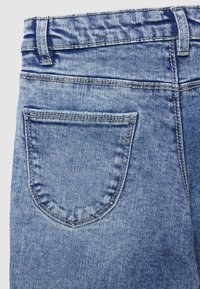 Jeans in denim di colore azzurro chiaro con una tasca posteriore a punta, cuciture visibili e una cintura con passanti. Texture liscia su tutta la superficie.