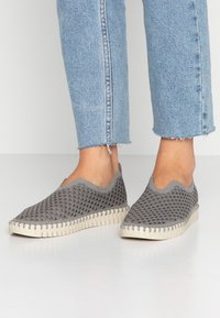 Scarpe slip-on grigie con tomaia in mesh testurizzato e suola rigata di colore chiaro. Progettate per il comfort con un taglio curvo alla caviglia.