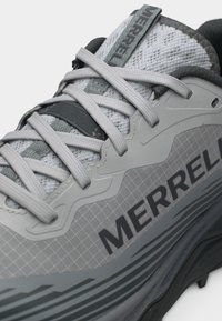 Κοντινή λήψη γκρι και μαύρου παπουτσιού Merrell με υφασμένους κορδόνια, γλώσσα από δίχτυ και έντονο λογότυπο στην πλαϊνή όψη.