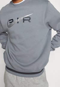 Grå crewneck sweatshirt i mjukt tyg, med en framträdande svart och silver Nike-logotyp i mitten, samt ribbade manchetter och nederkant.