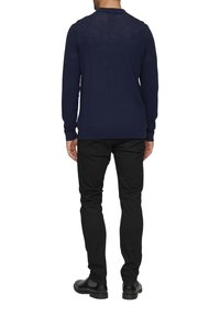 Navy modrý pulovr s dlouhým rukávem a límečkem, texturovaný úplet, v kombinaci s černými slim-fit kalhotami a černými botami, pohled zezadu.