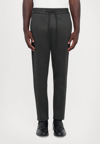 Pantalons de jogging gris foncé, texturés, avec une taille élastique et un cordon de serrage ajustable. Design à jambes fuselées, portés avec des mocassins noirs.