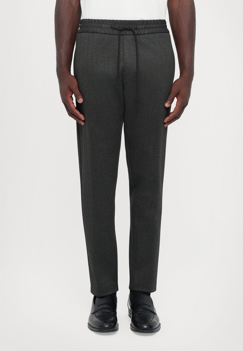 Mørkegrå, strukturerede joggerbukser med elastec bånd i taljen og justerbar snøring. Tapered ben design, båret med sorte loafers.