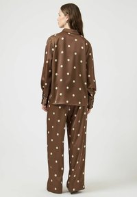 Ensemble chemise et pantalon à pois marron, en tissu lisse. Comprend des manches longues, un col et un pantalon ample.