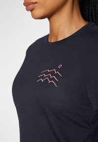 Camiseta de manga corta azul marino hecha de un tejido suave, con un gráfico de ola montañosa en rosa en el pecho. Cuello redondo y un corte relajado.