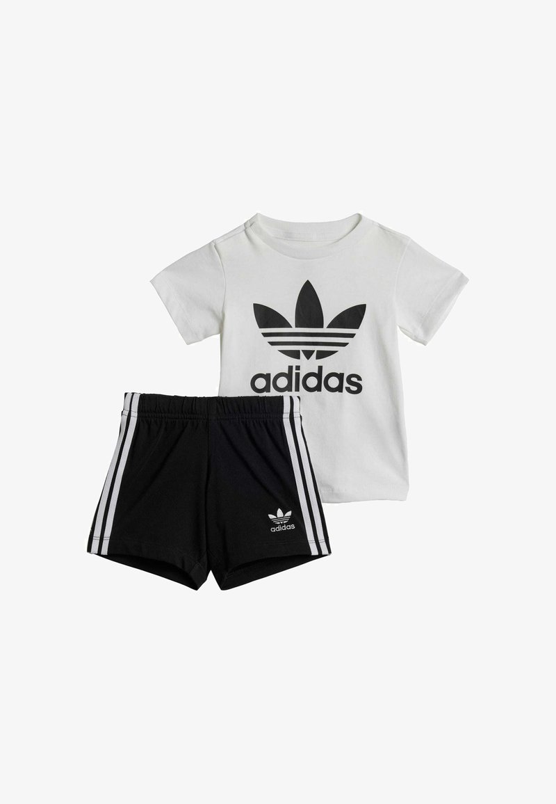 Adidas dječja odjeća koja se sastoji od bijele majice s crnim logotipom i crnih kratkih hlača s bijelim bočnim trakama te logotipom na rubu.